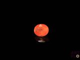 Une lune orange brille de mille feux dans le ciel nocturne et se reflète sur le sol.