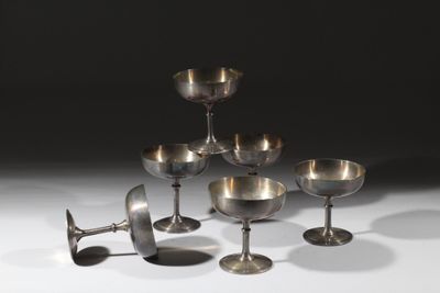 six verres à vin argentés et un verre à vin posés sur une surface blanche