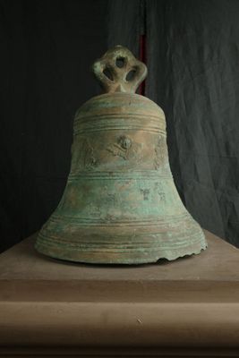 une grande cloche posée sur un socle, avec un drapeau en arrière-plan