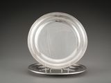 une assiette en argent posée sur un support à assiette en argent, sur un fond gris