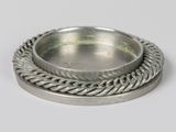 une assiette en argent entourée d'une corde torsadée sur un fond blanc