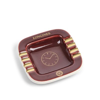 une photo d'un cendrier carré rouge et doré sur lequel figure une horloge