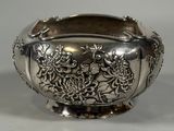 a silver bowl with flowers on it sitting on a table