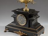 an antique black and gold clock with a bowl on top of it