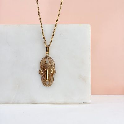 un collier plaqué or avec un pendentif en forme de visage posé sur un bloc de marbre