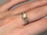 someone is holding a ring with a pearl on it