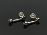 une paire de boucles d'oreilles en argent et émeraude posées sur un fond noir