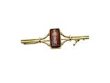 a close up of a gold tie bar with a red stone on it