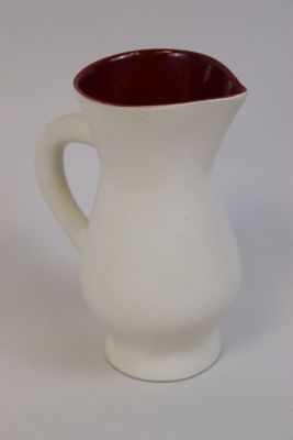 un pichet blanc avec une anse rouge posé sur une table blanche