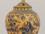 a blue and yellow vase on a table with a light on it
