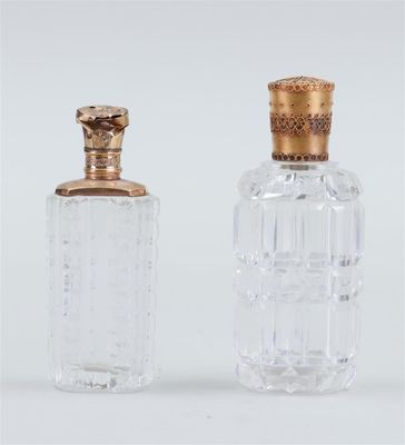 deux bouteilles en verre transparent avec des bouchons dorés, posées sur une surface blanche