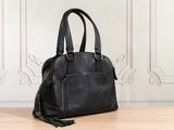 black leather handbag sitting on a wooden floor in front of a white wall