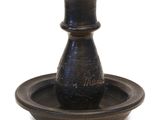 un vase noir posé sur une assiette, sur une surface blanche