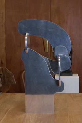 une sculpture en métal posée sur une table en bois, avec un chien en arrière-plan