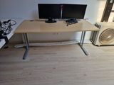 un bureau avec deux écrans et un ventilateur dans un coin