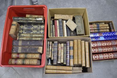 Plusieurs cartons remplis de vieux livres sont posés les uns à côté des autres sur le sol.