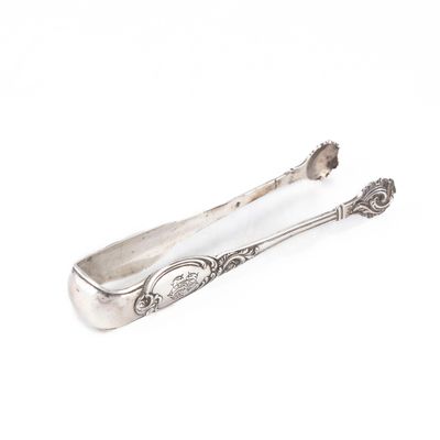une cuillère ancienne en argent et son repose-cuillère posés sur une surface blanche