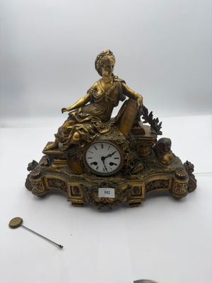 a gold clock with a woman sitting on it
