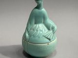 a small blue vase with a woman sitting on it