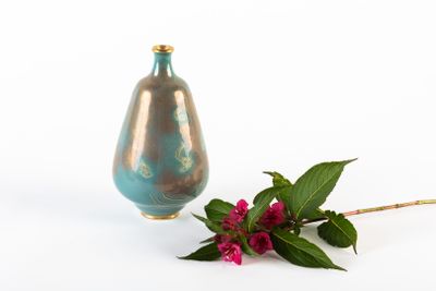 un vase bleu et une fleur rose sur un fond blanc