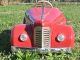 a red toy car sitting in the grass in front of a fence