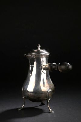 une cafetière ancienne en argent posée sur un support, sur fond noir