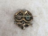 a small brooch with a green stone in it