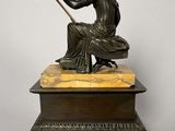 an antique bronze statue of a woman sitting on a marble pedestal