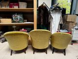 three yellow chairs sitting in front of a wooden shelf filled with clothes