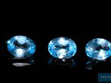 three blue topazte gems sit side by side on a black surface