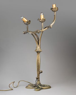 un chandelier ancien en laiton à trois bougies, posé sur un socle