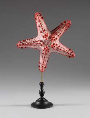 une photo d'une sculpture représentant une étoile de mer rouge posée sur un socle noir