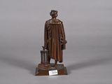 bronze statue of a man with a hat and coat holding a suitcase