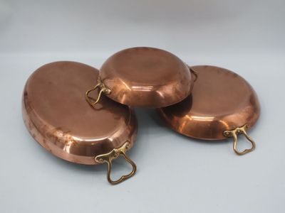 trois casseroles en cuivre empilées les unes sur les autres sur une table