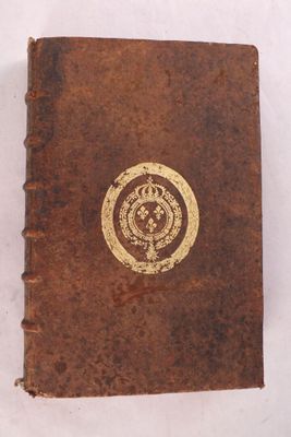 un vieux livre orné d'un emblème doré posé sur une surface blanche