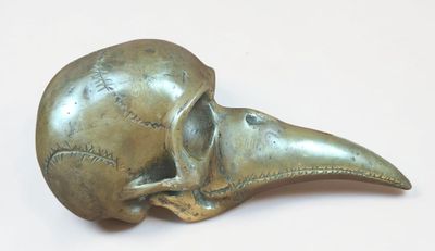a bronze bird skull on a white surface