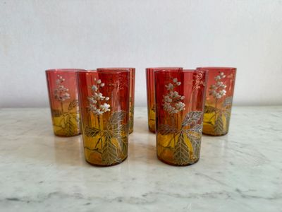 four red glasses with gold designs on them sitting on a marble surface
