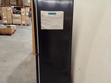 a large black refrigerator in a warehouse with boxes in the background