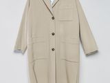 Un manteau beige est suspendu à un cintre contre un mur blanc