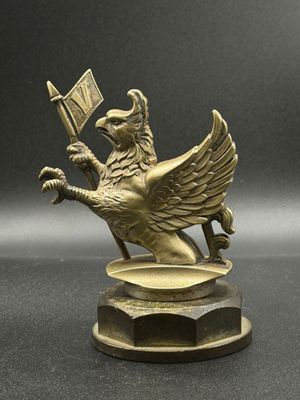 statue en laiton représentant un oiseau tenant un drapeau, posée sur un socle