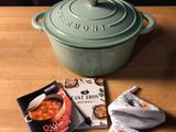 a pot of soup next to a pair of oven mitts and a book on a table