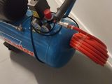 a blue air compressor sitting on the floor next to a red hose