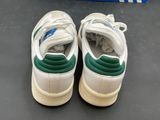 pair of white and green sneakers on a black surface with a blue box in the background
