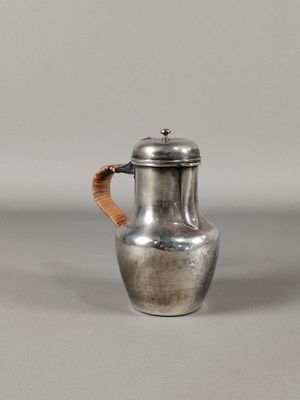 une cafetière ancienne en argent, dotée d'une poignée en bois sur un fond gris
