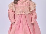an old fashioned doll with a pink dress and hat on a stand