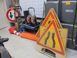 un panneau jaune et rouge posé par terre à côté d'une pile de cônes orange