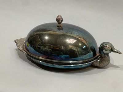 a silver plate with a bird on it on a white surface