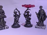 quatre statues en bronze représentant des personnages et une fleur sur fond blanc