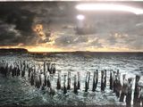 tableau représentant un coucher de soleil sur un plan d'eau d'où émergent des poteaux en bois