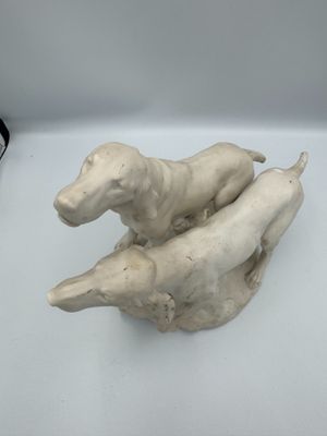 sculpture représentant deux chiens assis l'un sur l'autre sur une surface blanche